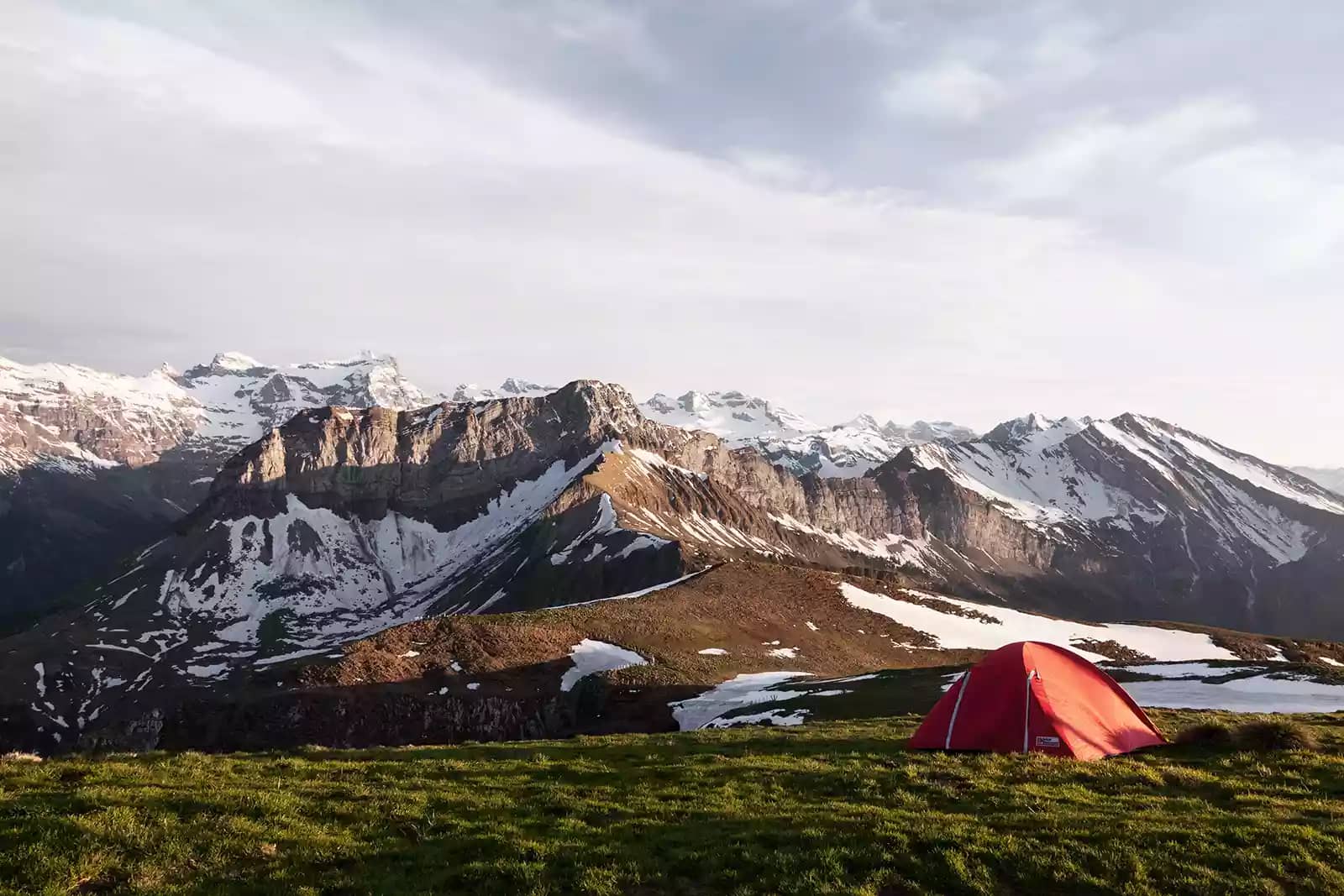 red tent in an open field camp spot beside a mountain range