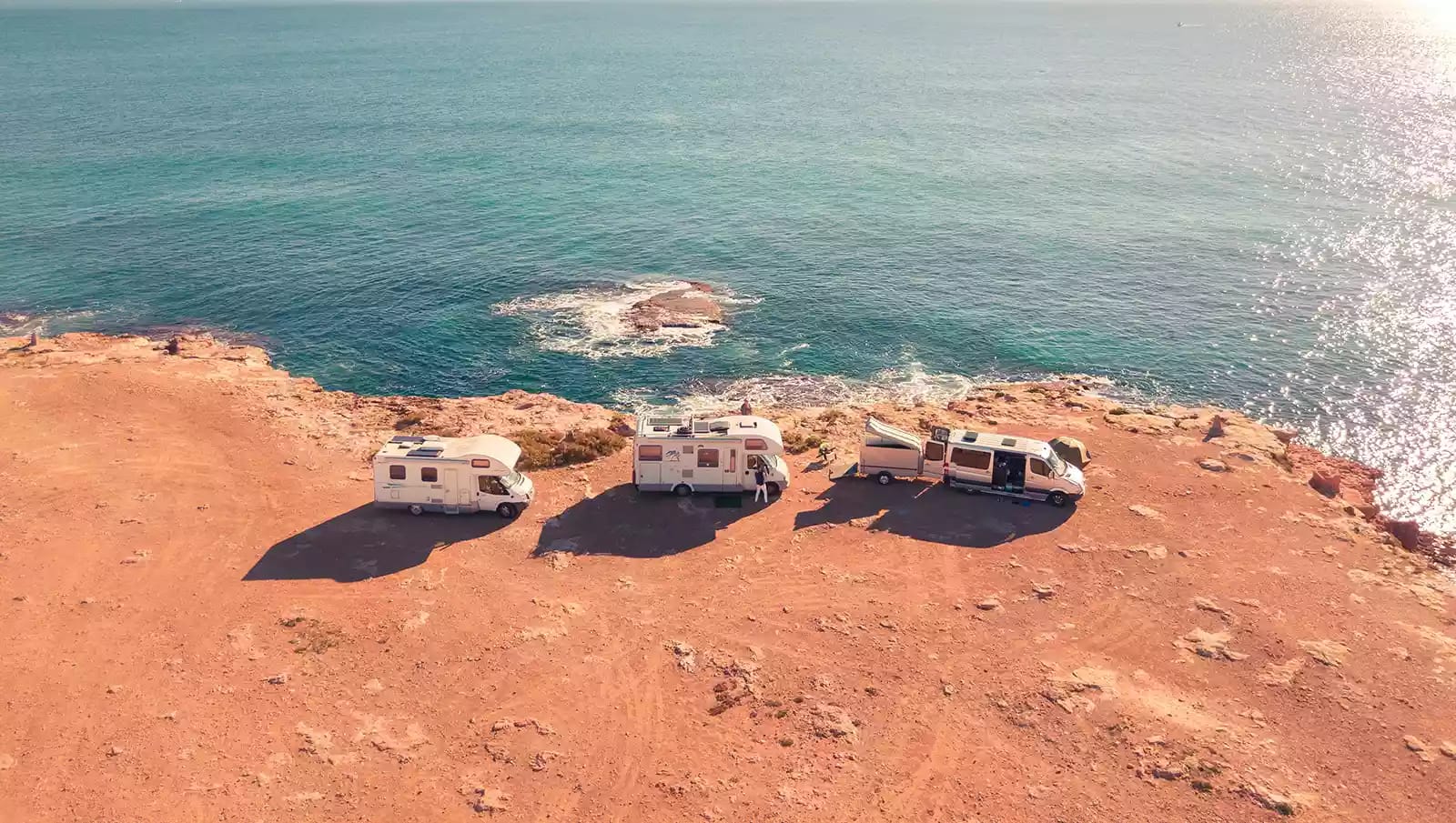 three white RVs lined up next to the ocean