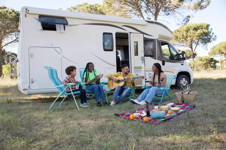 four people sitting outside an RV playing guitar