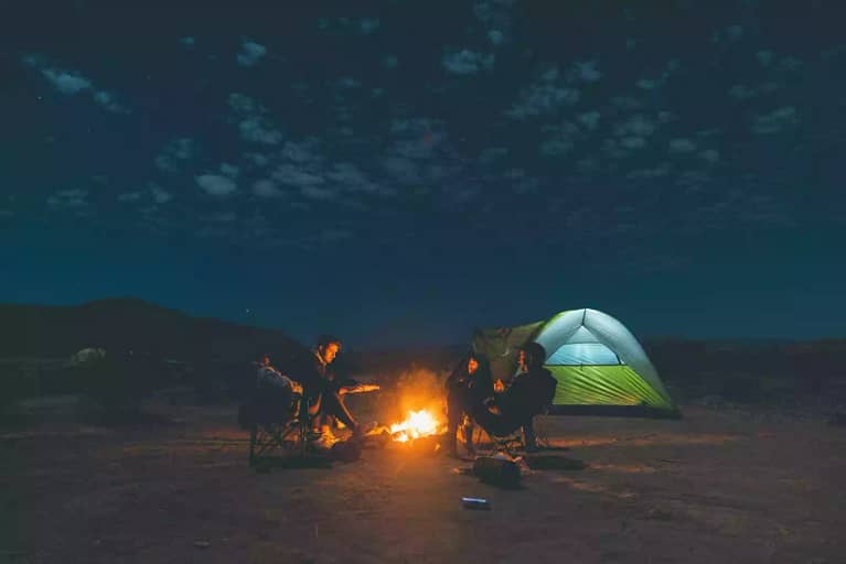 A group of people around an evening campfire, next to a tent set up for camping in Texas at Big Bend National Park