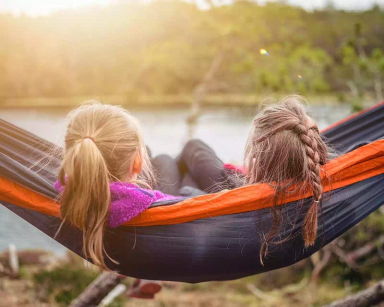two kids with ponytails sitting in a hammock outside