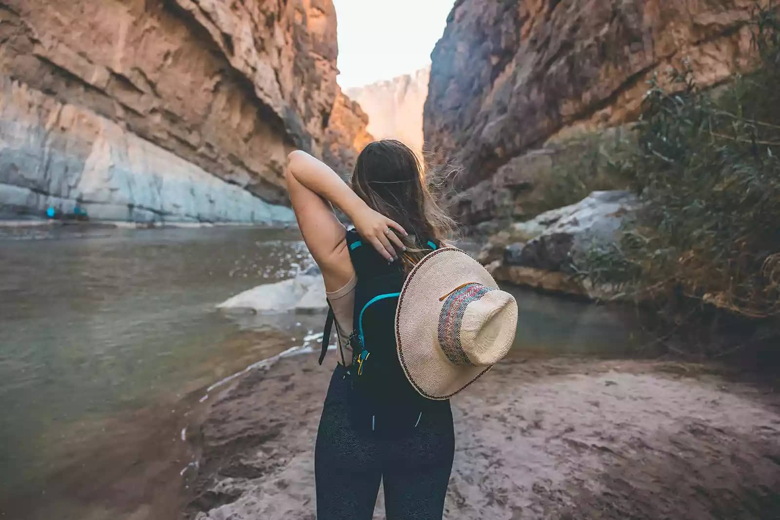 woman with brown hat standing at river between canyons