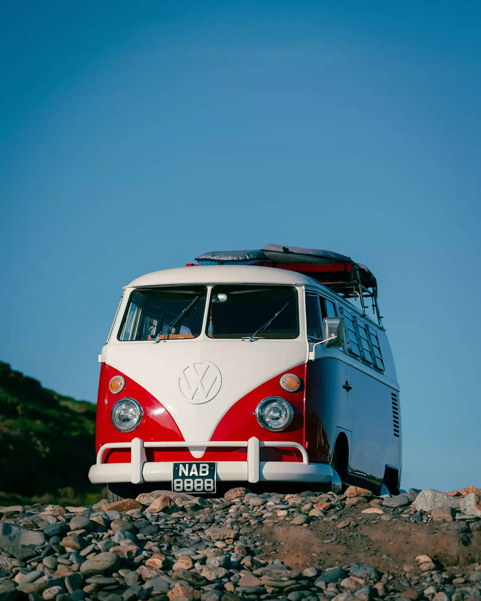 A red and white VW camper van is parked near a rocky shoreline with a deep blue sky overhead.