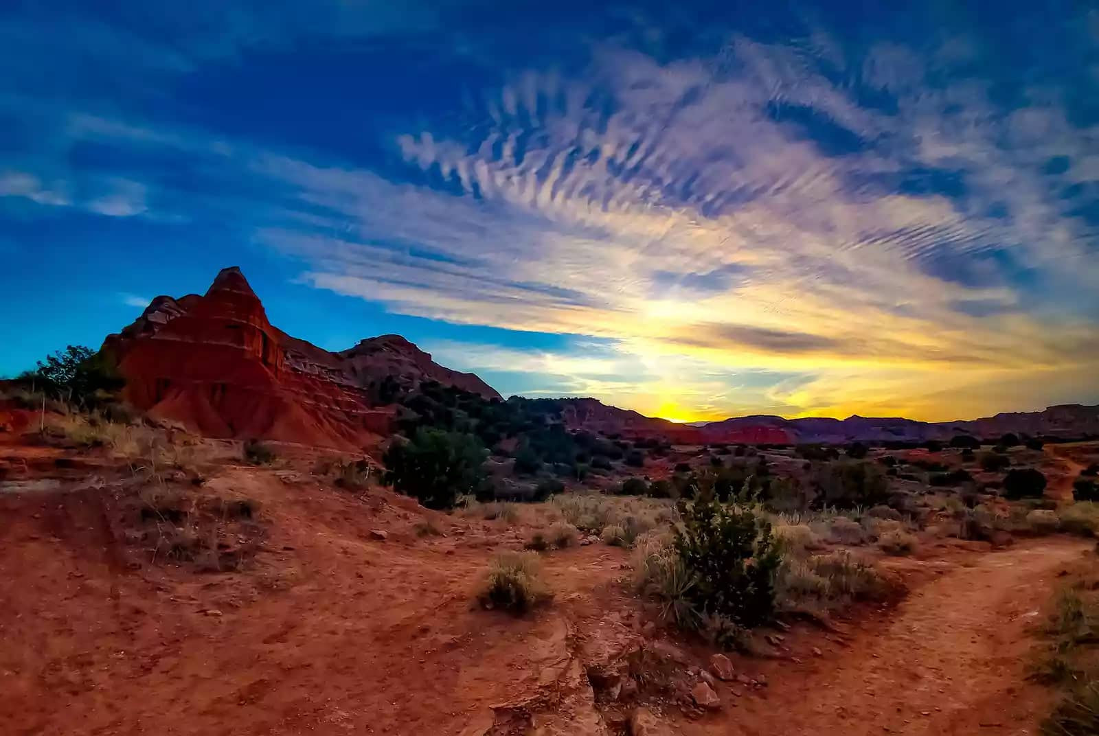 The rugged landscape of Palo Duro Canyon, a scenic stop on a Texas road trip, under a bright blue sky with illuminated clouds