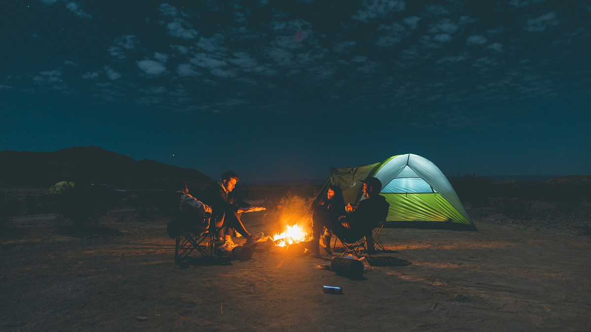 Two couples camping under the stars at night and talking around a campfire in their camping chairs; camping tips. Photo taken by Caleb Fisher.