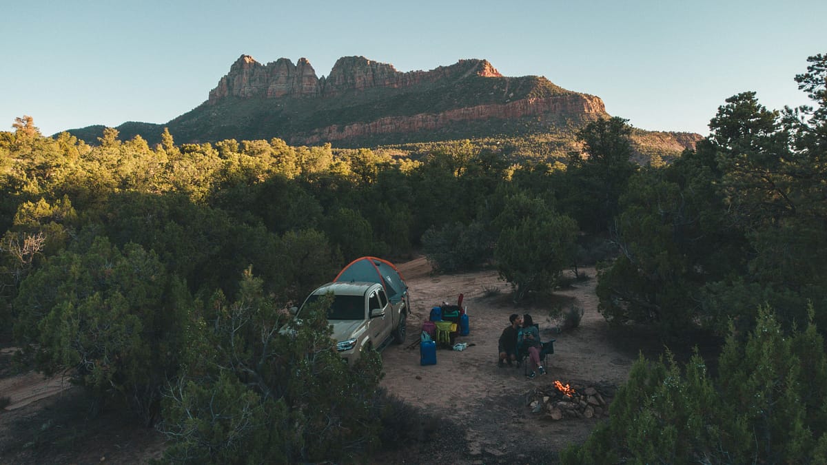 Man and woman at their private camping site in Zion National Park with their truck, their tent set up, kissing and enjoying themselves by the fire pit. Photo by Katie Musial.