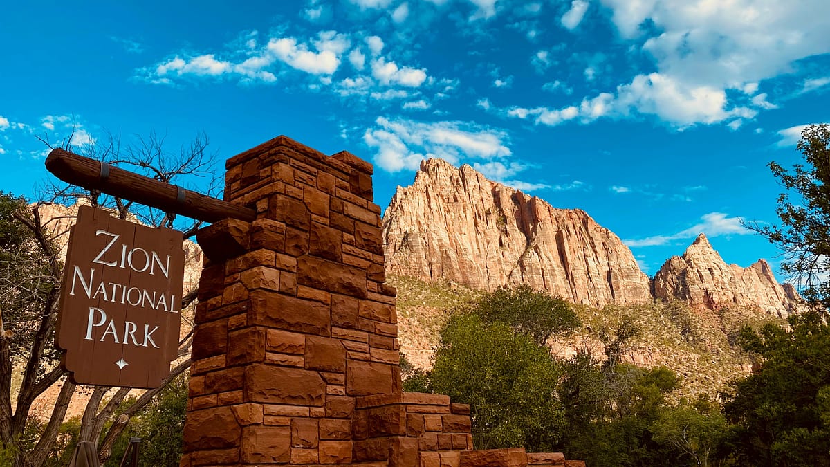 The Zion National Park sign by the visitors center of the park with a grand landscape in the background. Photo taken by Charlie Wollborg.