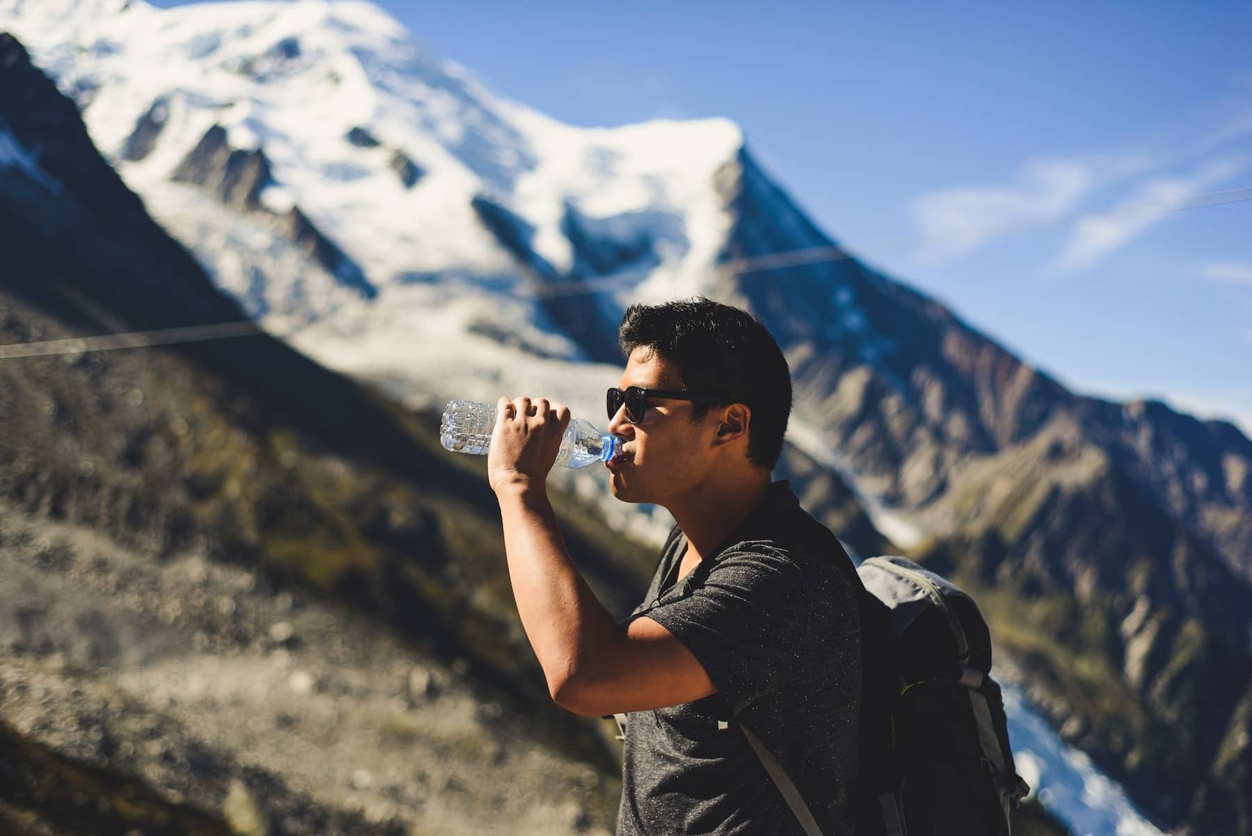 Man drinking water on a hike with mountains in background to convey tips for staying hydrated