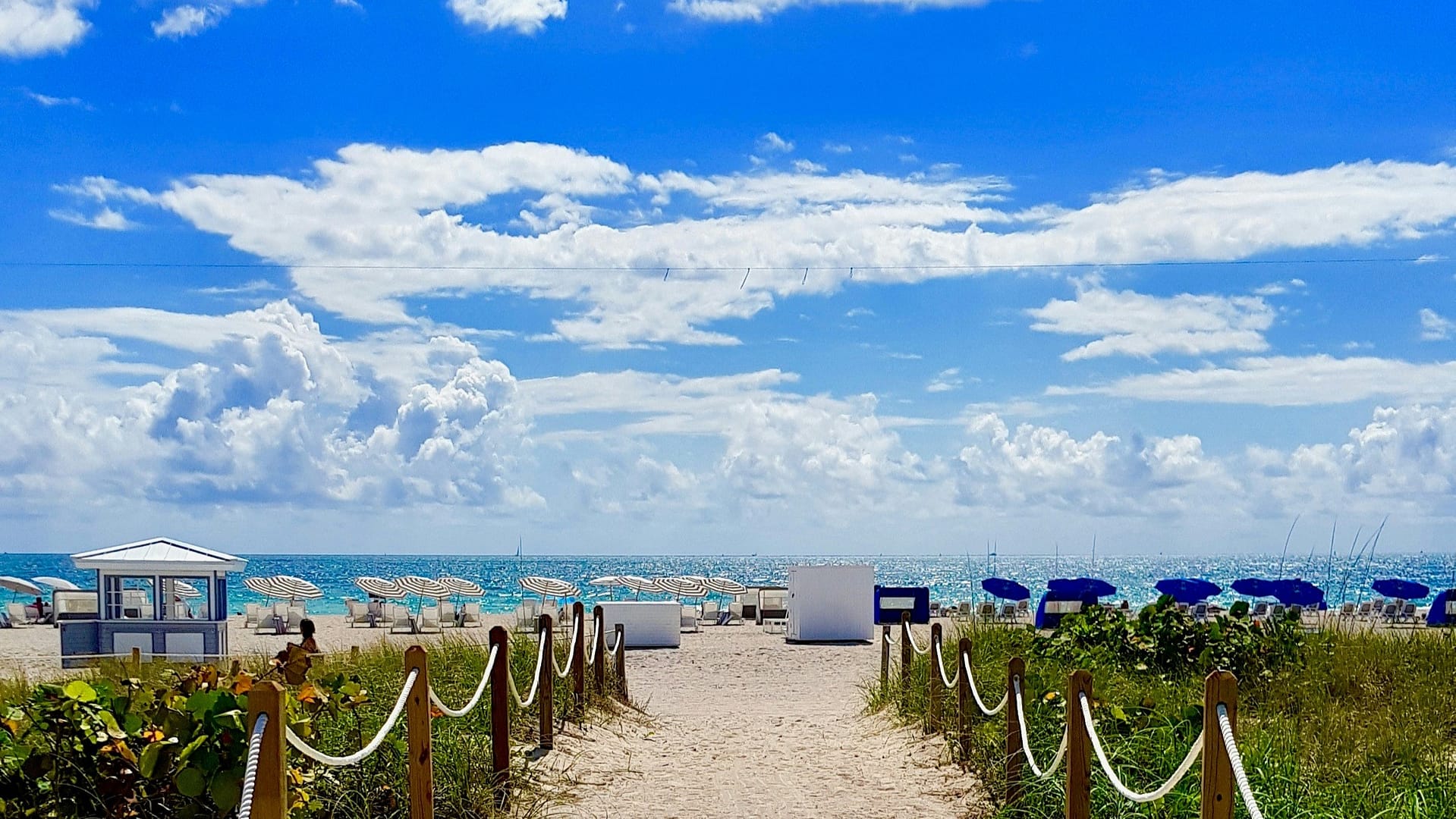 A sandy pathway under a cloudy deep blue sky leading to a Florida beach near one of the best RV sites in Florida. Photo by Pedro Bariak.