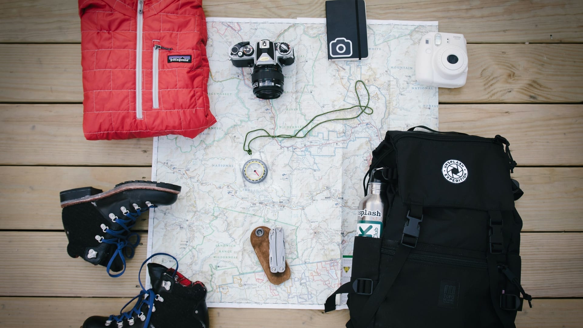 Camping suppliers like a backpack and compass spread out on a table over a map getting ready to head out into nature.