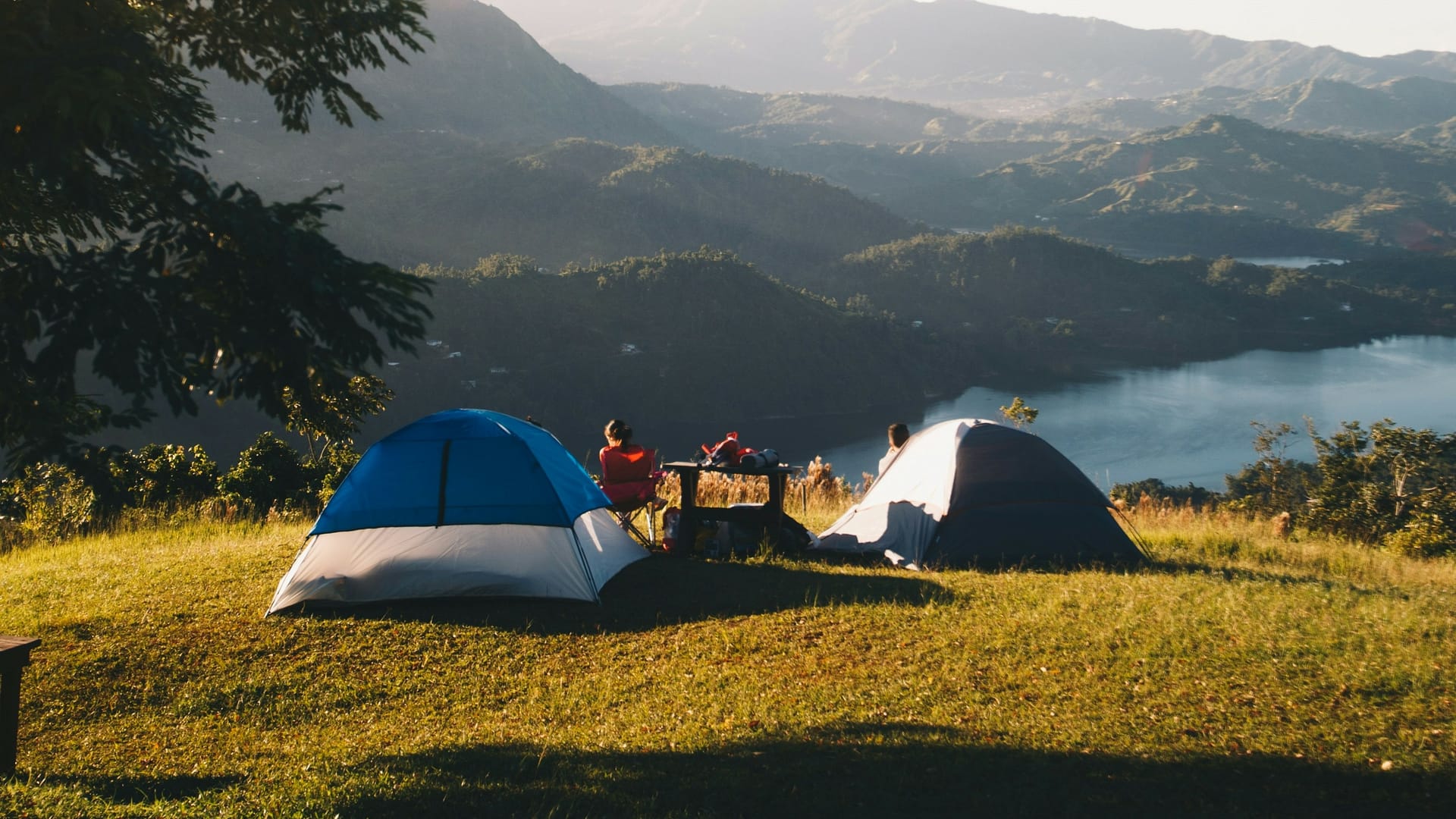 Two people and two small tents camping etiquette on top of a green hill overlooking a huge wide open landscape below. Photo by Victor Larracuente
