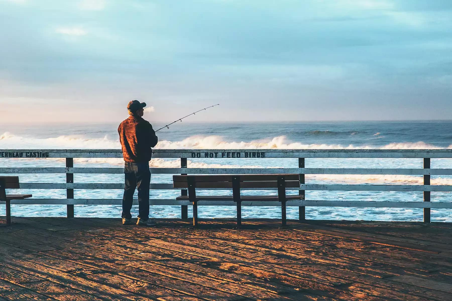 man fishing on an ocean pier during the day