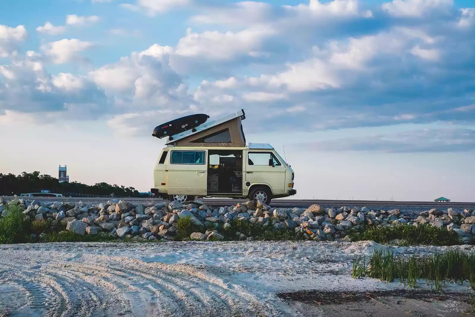 A pop-up camper van with an open side door is set up for camping on a beach in Florida.