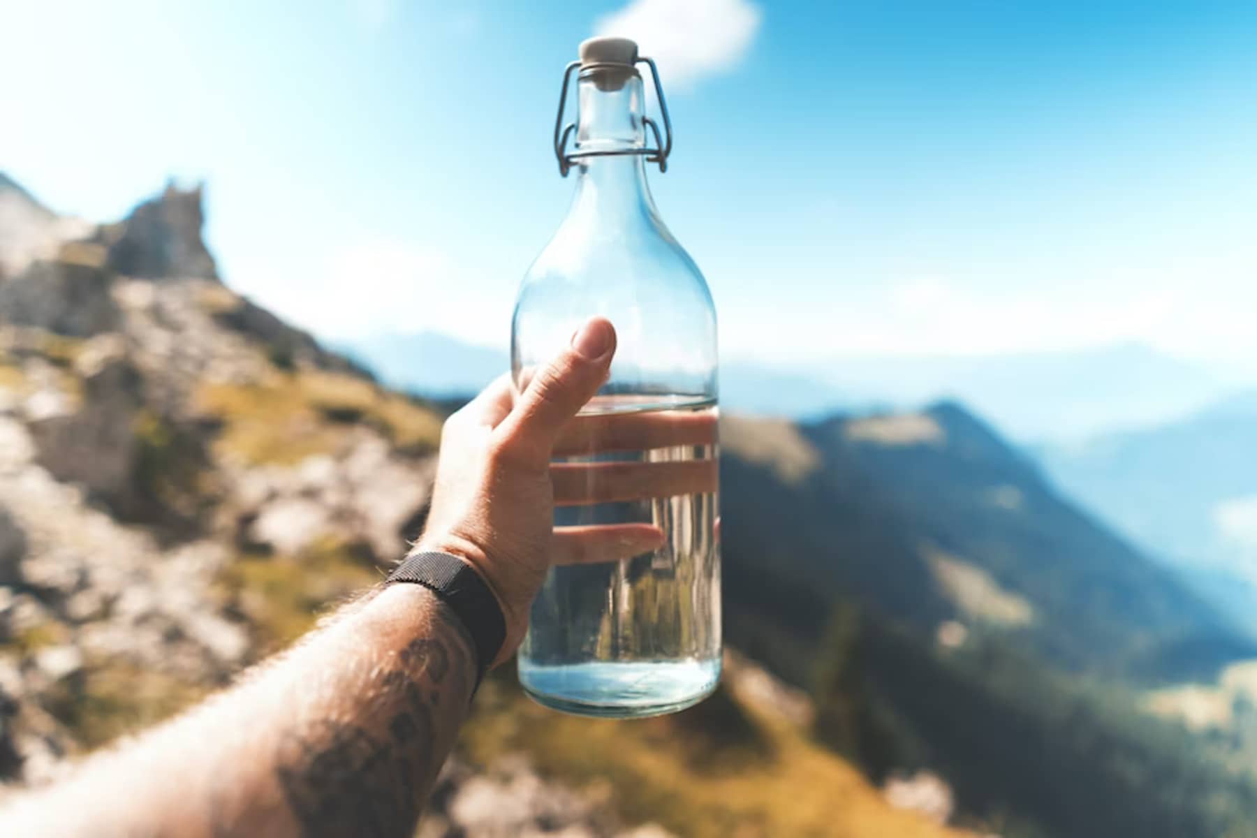 Holding a bottle of water with mountains in backdrop to convey hydration tips for summer