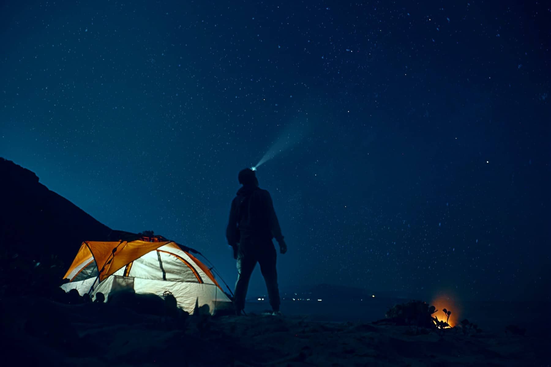 image of man star gazing at night by a camp to convey what astro tourism is