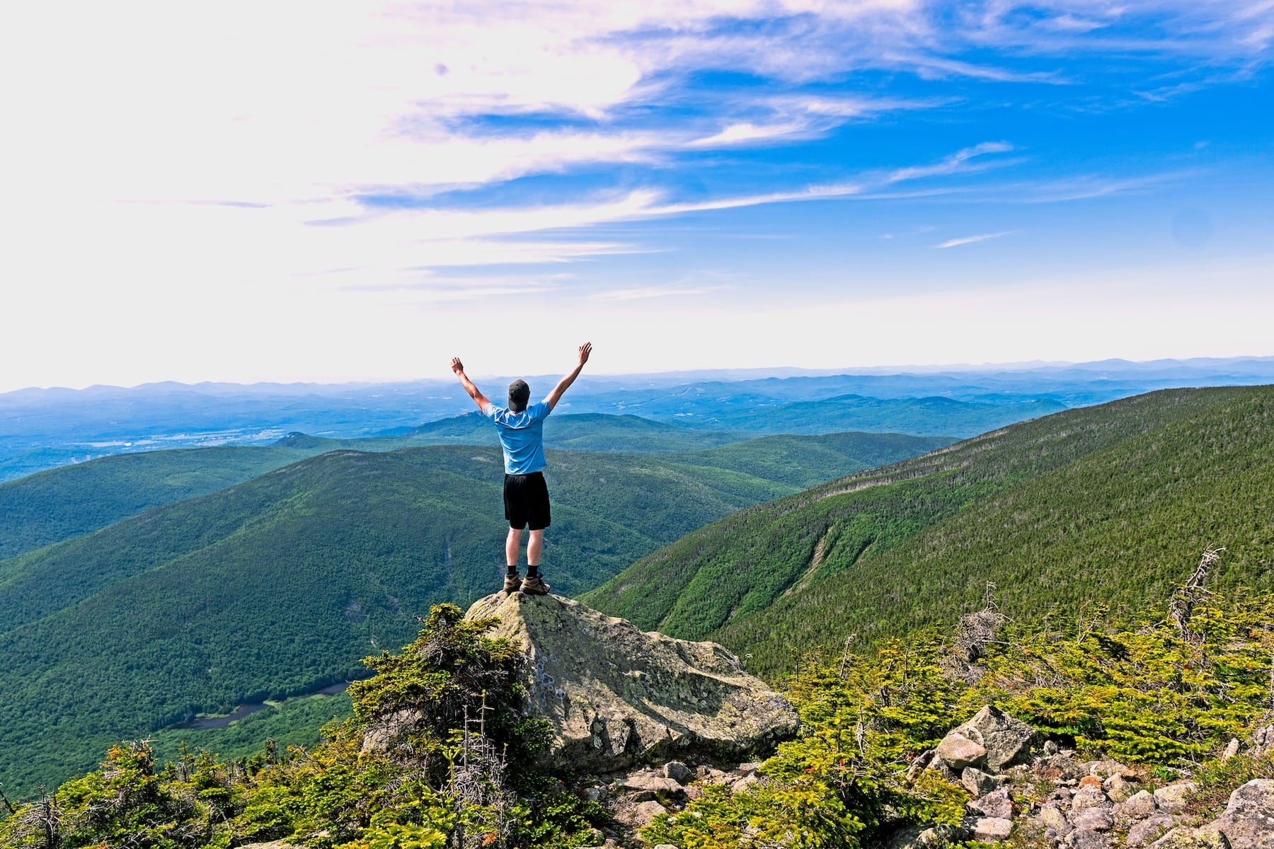 man doing a victory pose while hiking on a mountain to convey the science of being happy and healthy outside
